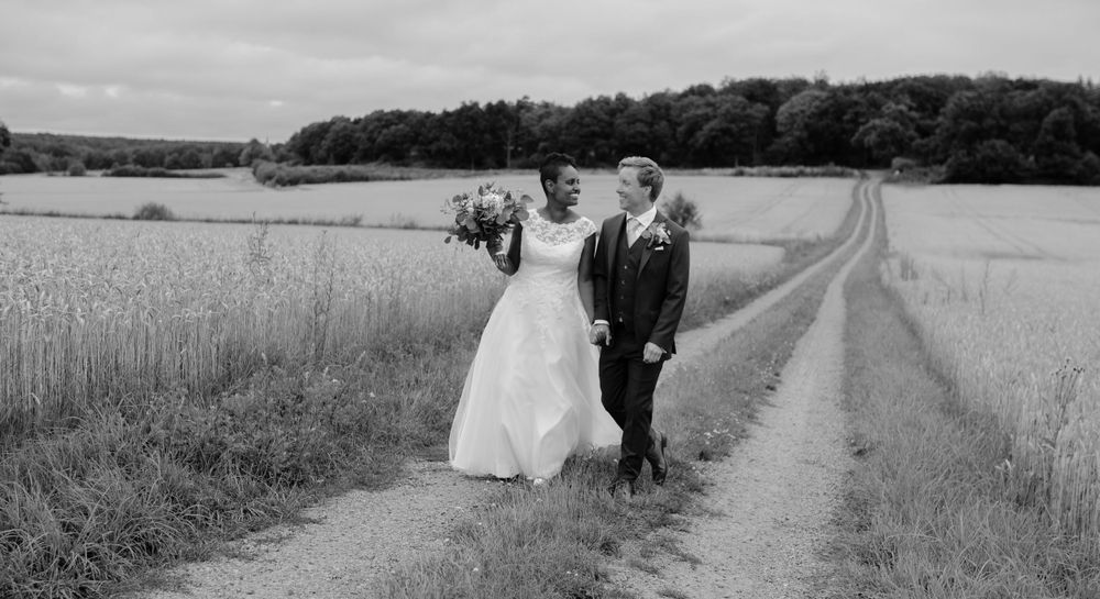 A couple walking down a rustic dirt path through wheat fields on their wedding day.