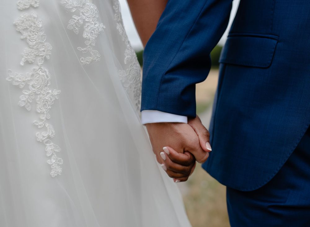 Close-up of bride and groom holding hands, showing white dress and navy blue suit details.