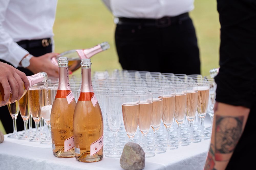 Pink champagne being poured into glasses on an outdoor serving table.