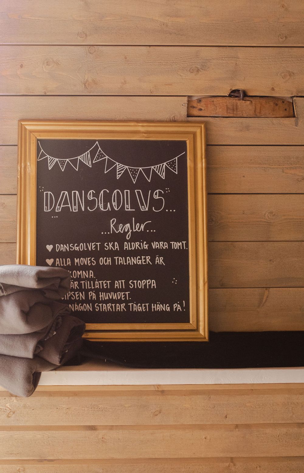 A chalkboard sign with text and bunting drawings mounted on a wooden wall.