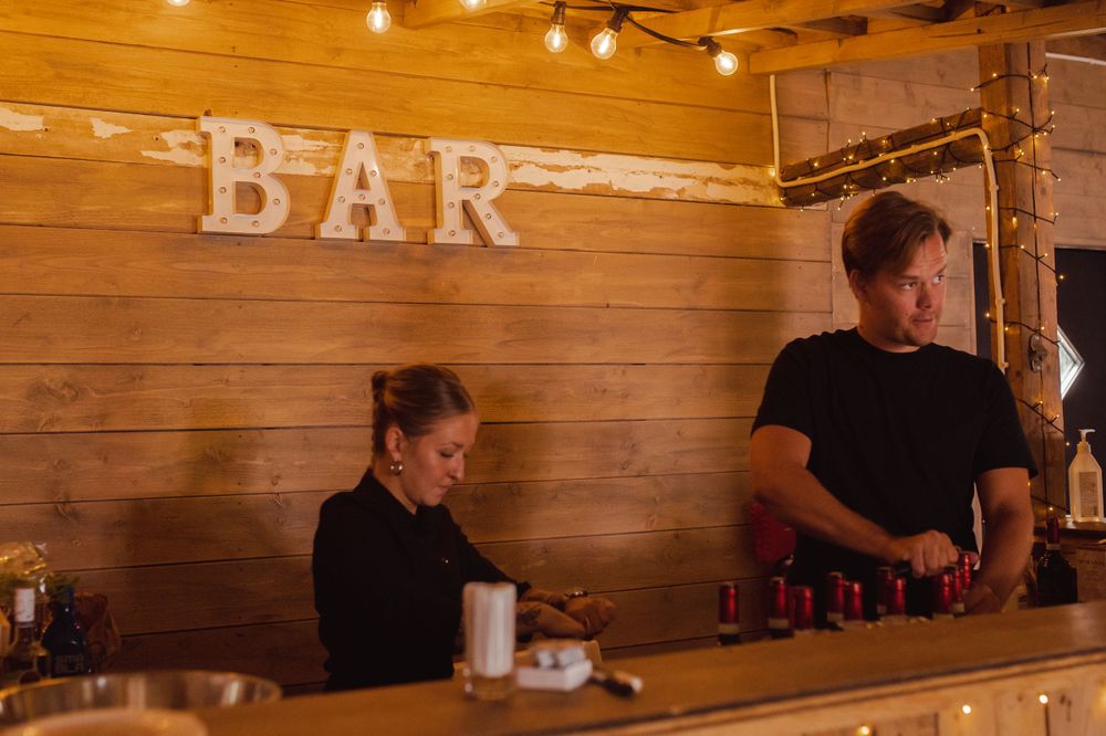Rustic wooden bar setup with bartenders preparing drinks under warm lighting.