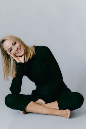 Casual studio portrait showing relaxed pose in black sweater against light grey backdrop.