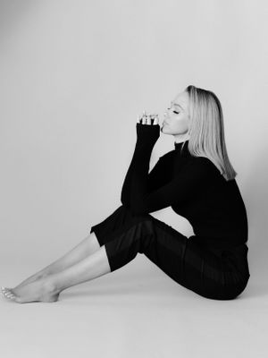 Artistic black and white profile shot featuring contemplative pose in dark outfit against light background.