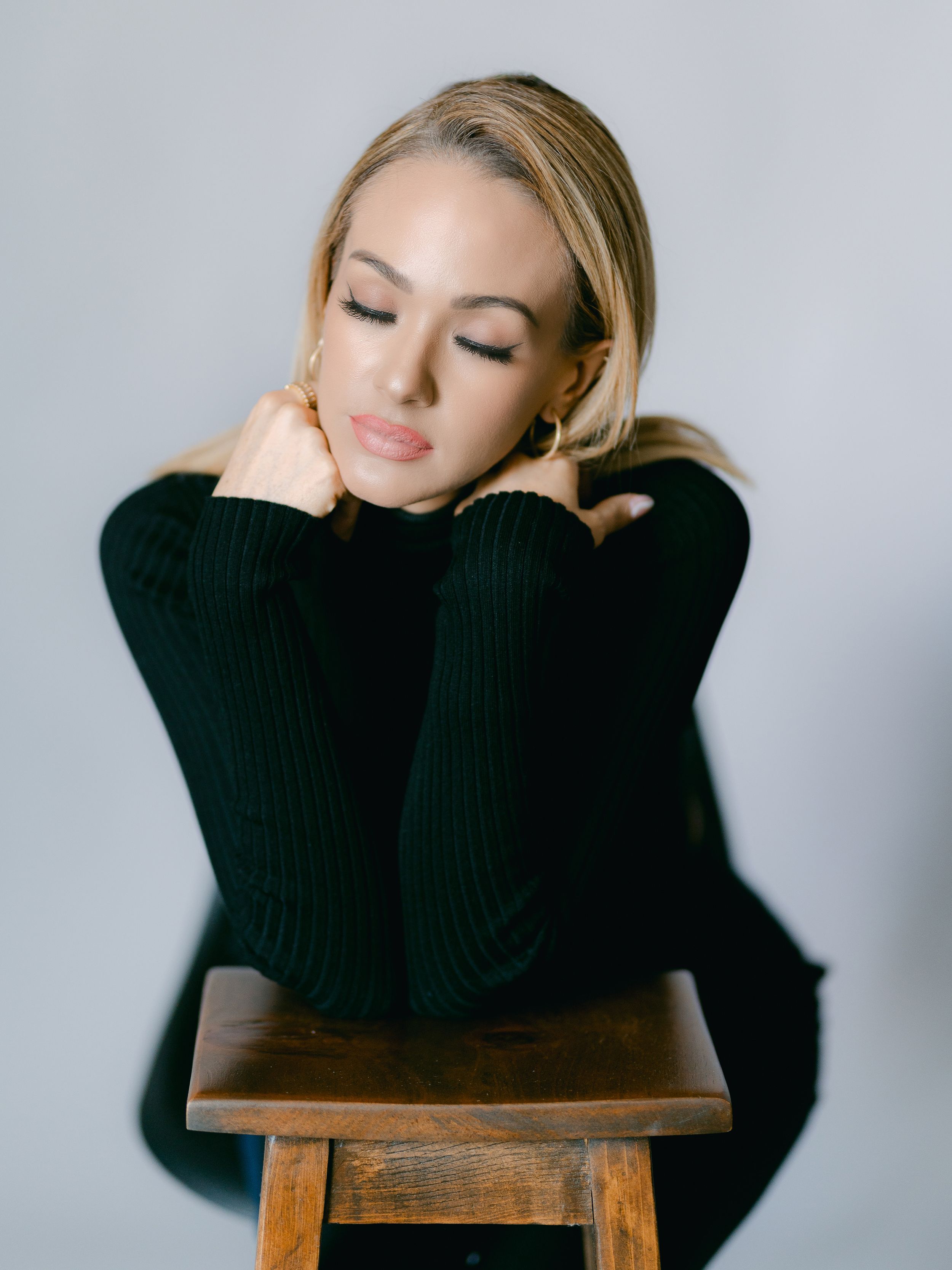 Intimate black and white portrait showcasing contemplative pose on wooden stool wearing dark sweater.