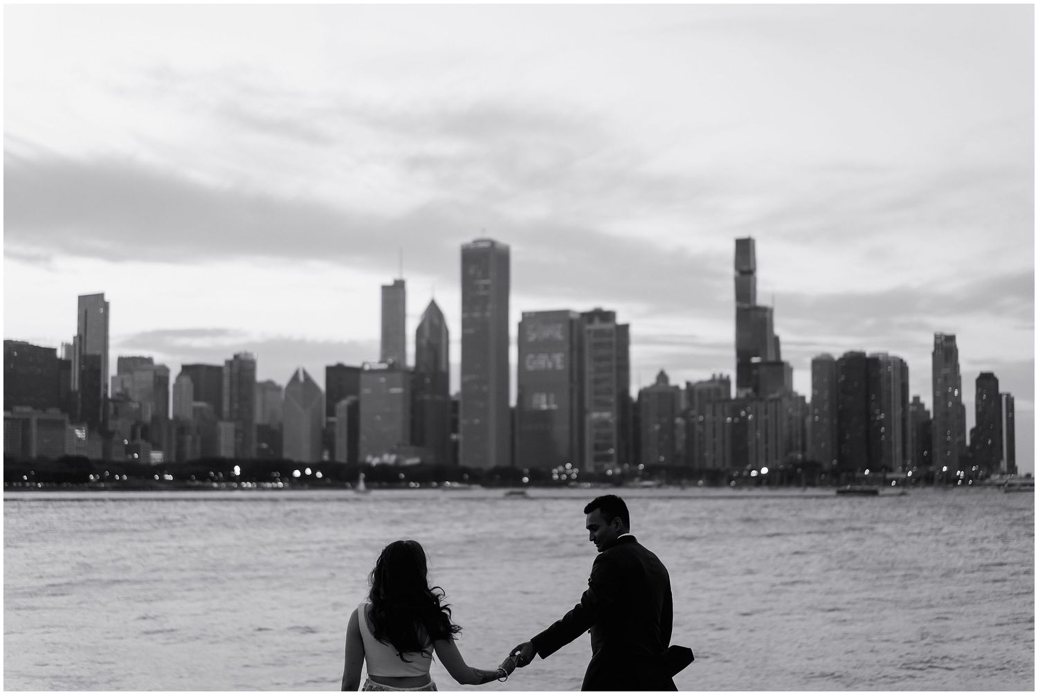 Black and white silhouette of a couple holding hands against Chicago's dramatic skyline.
