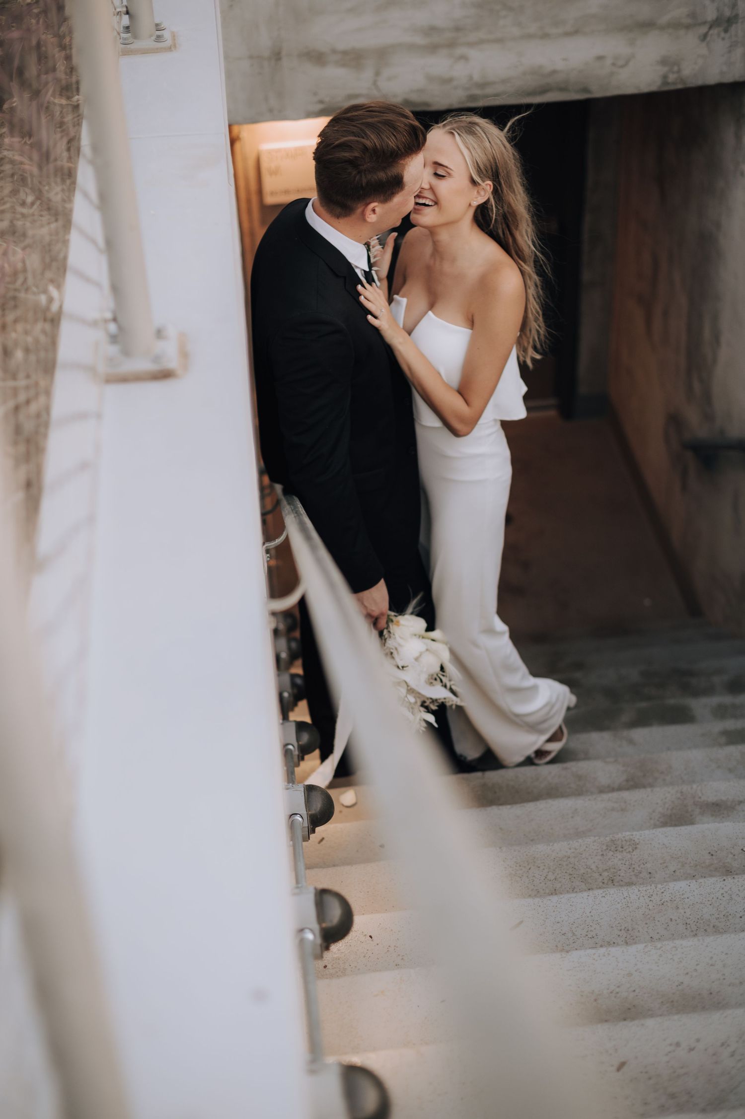 Wedding couple sharing a tender moment on white staircase with ambient lighting.