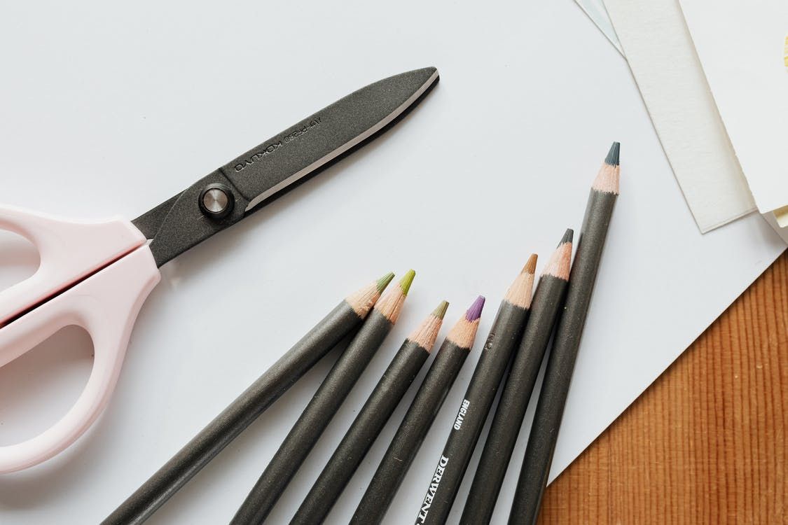 Pink scissors and pencils on a white surface with paper, representing crafting or office supplies.
