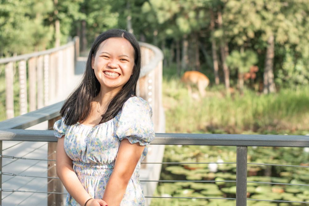 Person in a floral dress smiles joyfully against a backdrop of lily pads and water.