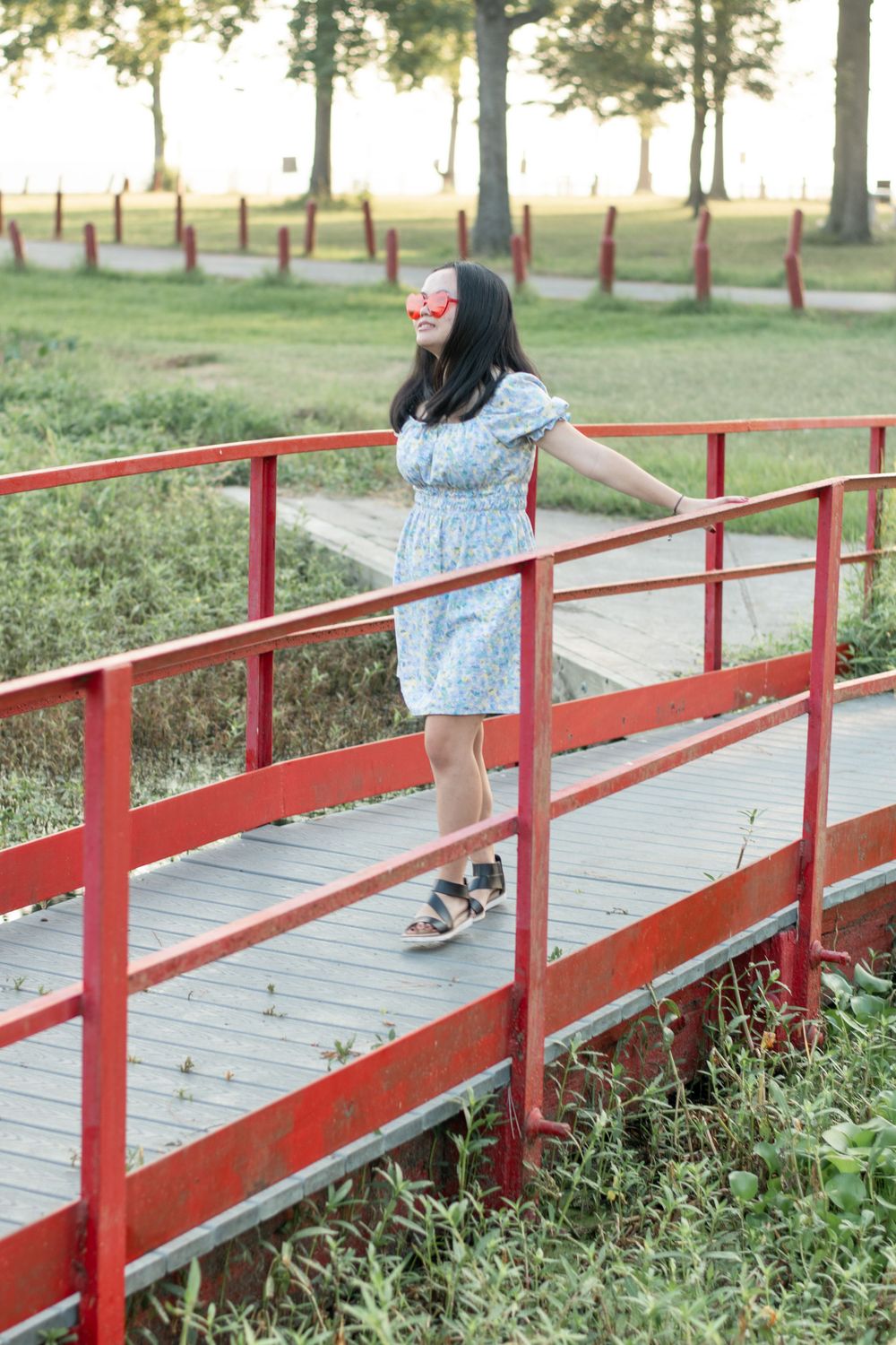 A person in a floral dress stands on a red-painted bridge during golden hour.
