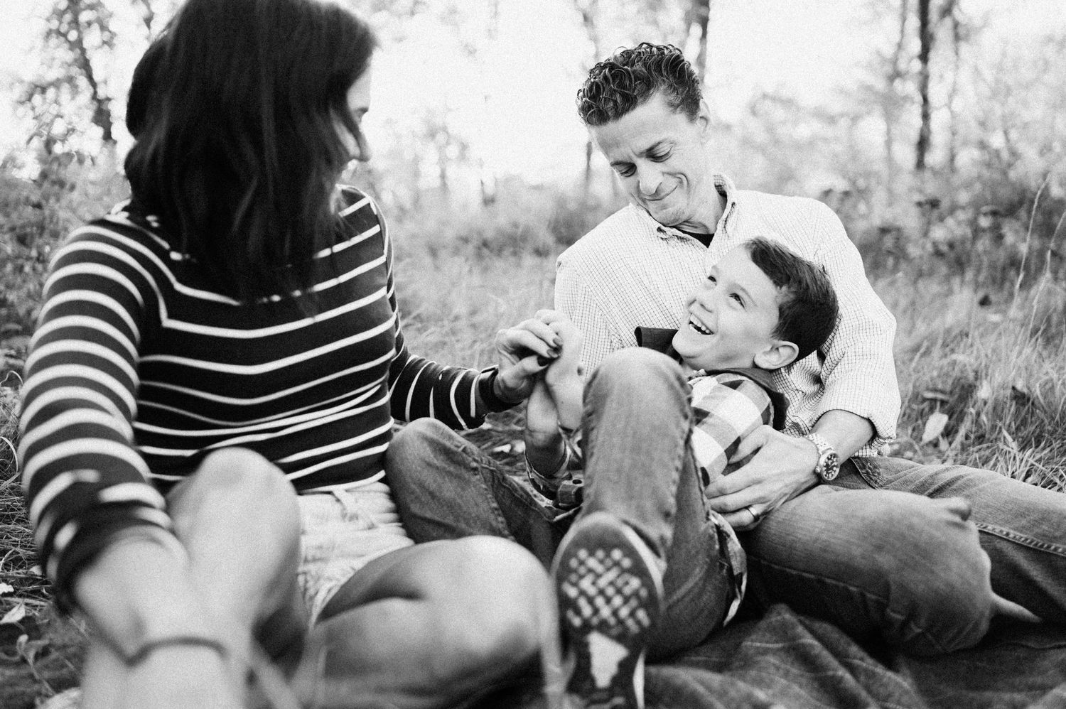 Black and white candid photo of three people relaxing together outdoors on grass in casual clothing.