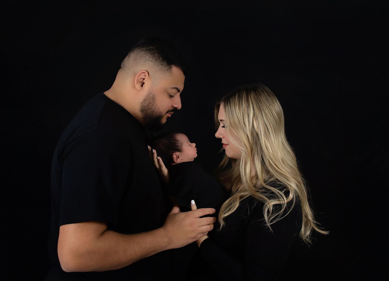An intimate family portrait against a black background in dramatic lighting.
