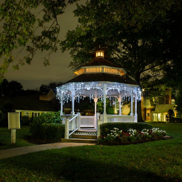 Illuminated white gazebo decorated with string lights glows beautifully at night in a garden setting.