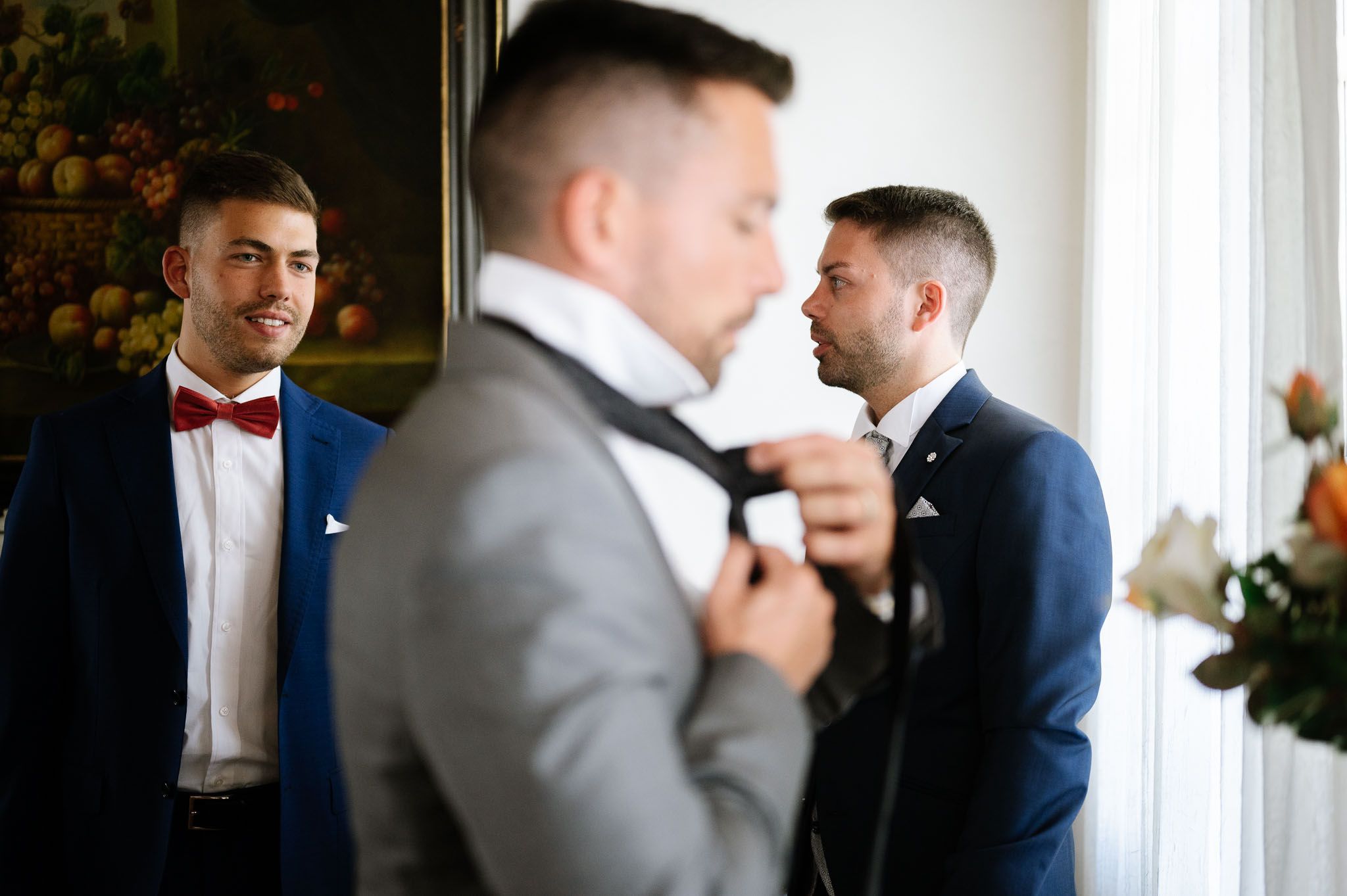 Wedding preparation scene reflected in mirror showing formal attire adjustments.