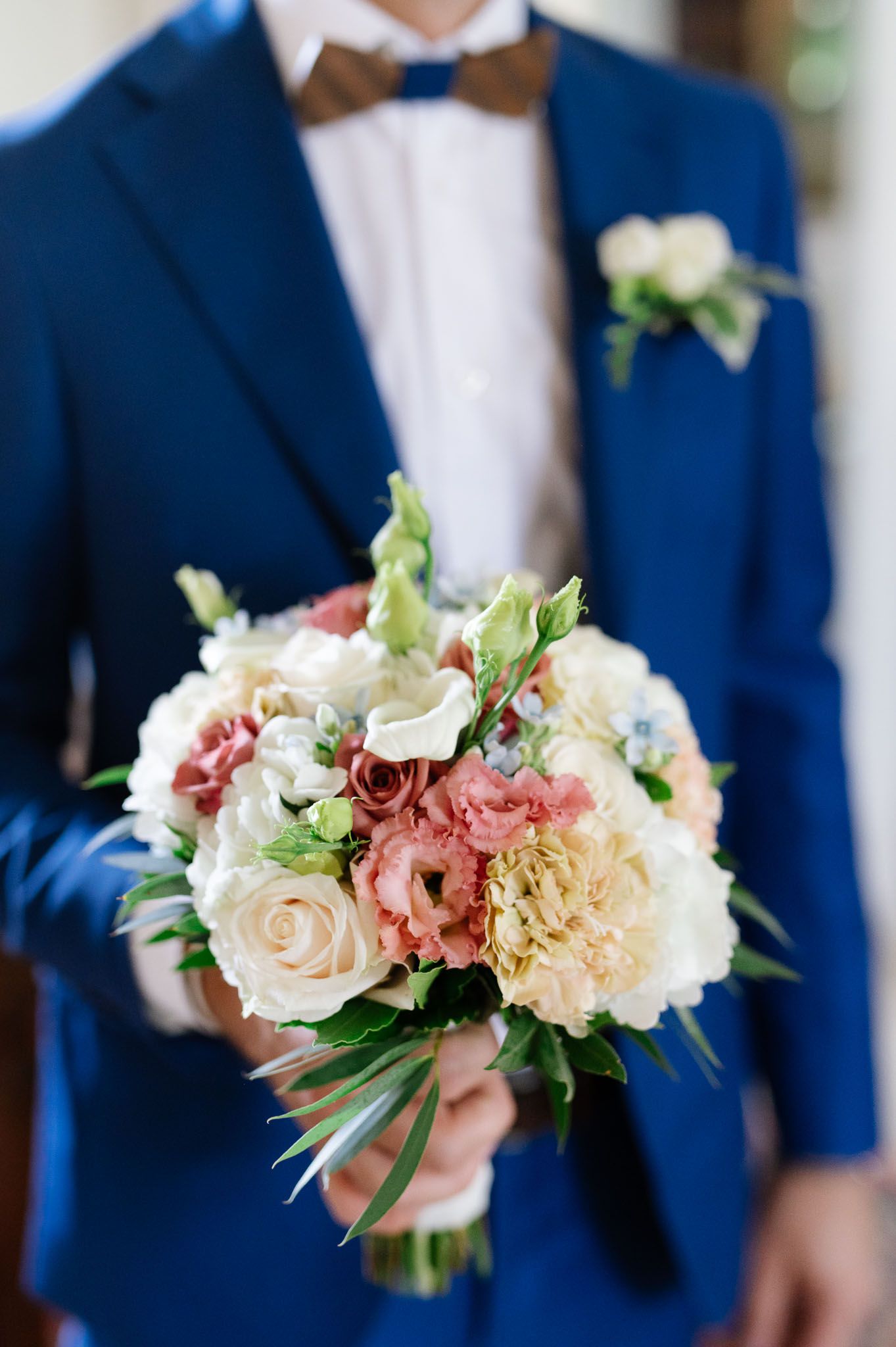 A delicate bouquet of pink and cream roses held against a navy blue suit with brown bow tie.