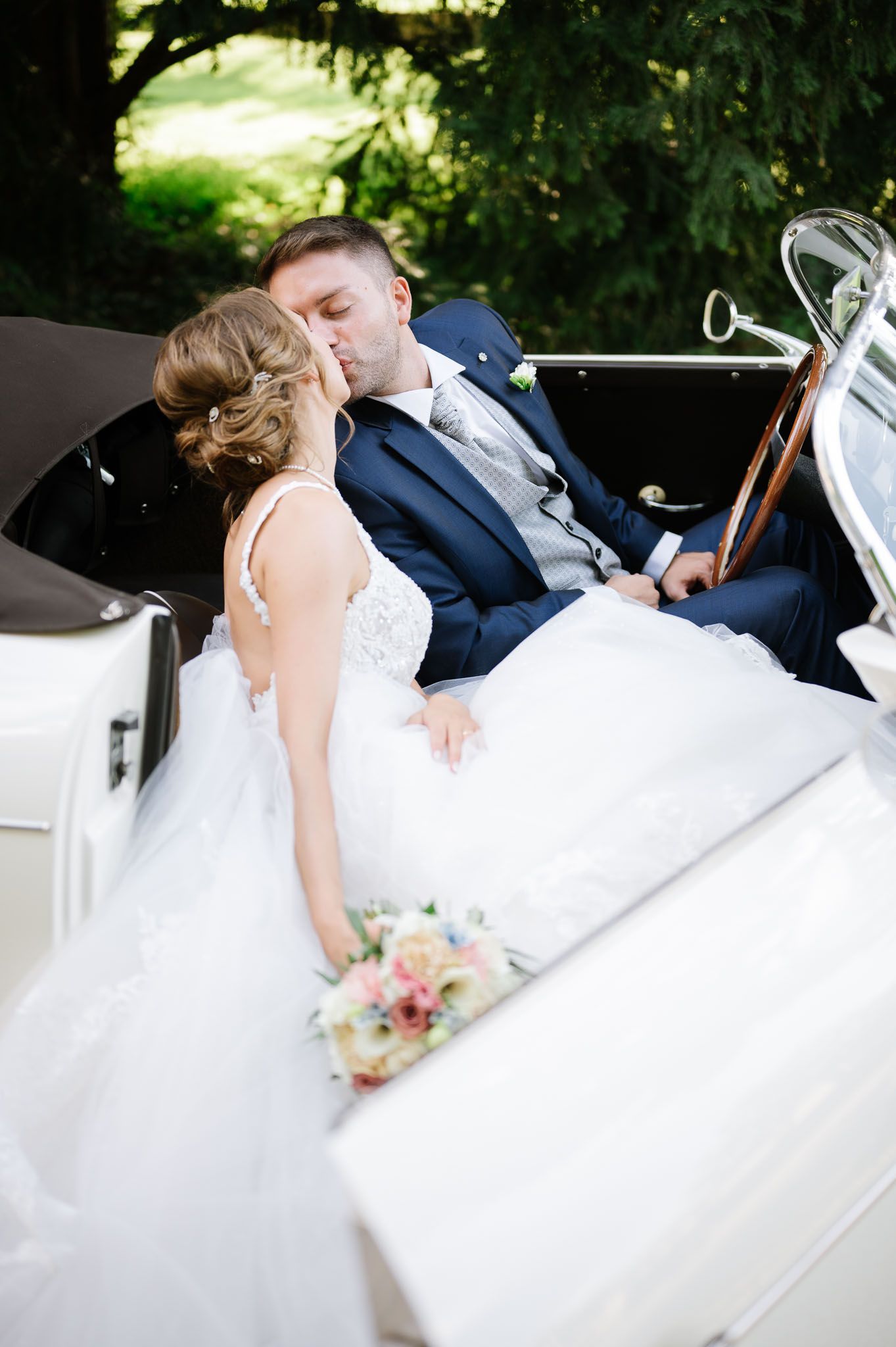 Couple sharing a romantic moment in a vintage white car on their wedding day.