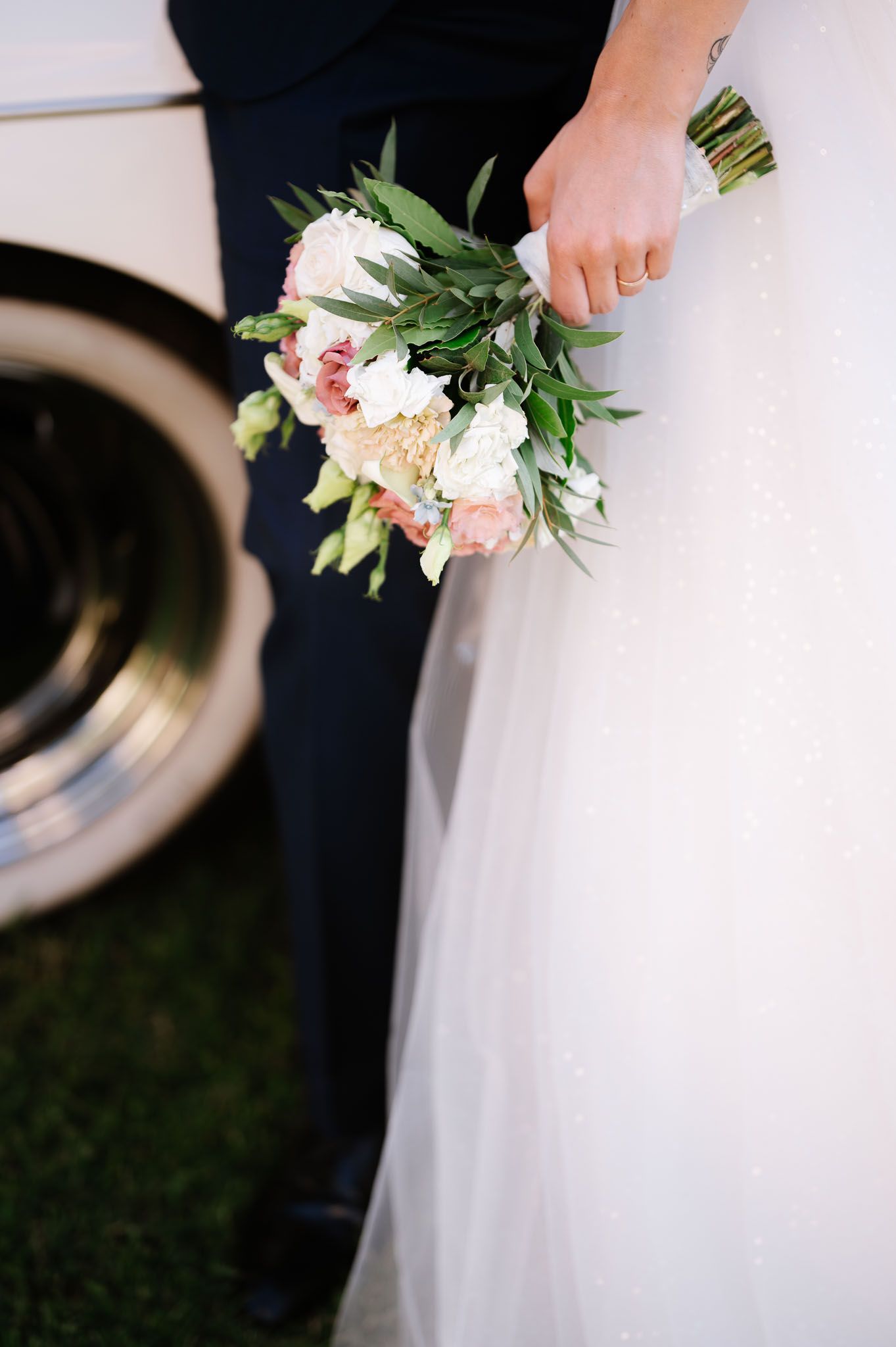 Wedding bouquet with pink and white flowers held against formal attire.