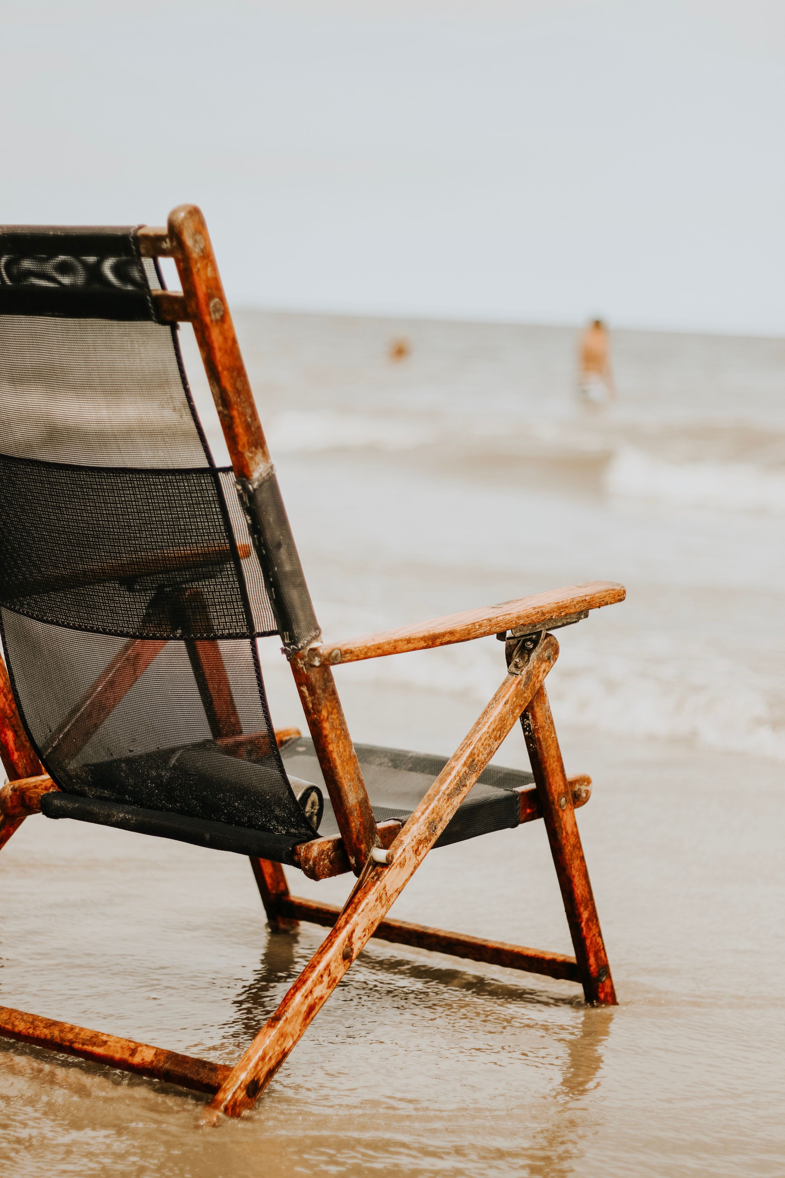 Close up of a rustic beach chair sitting in shallow ocean water at the shoreline.
