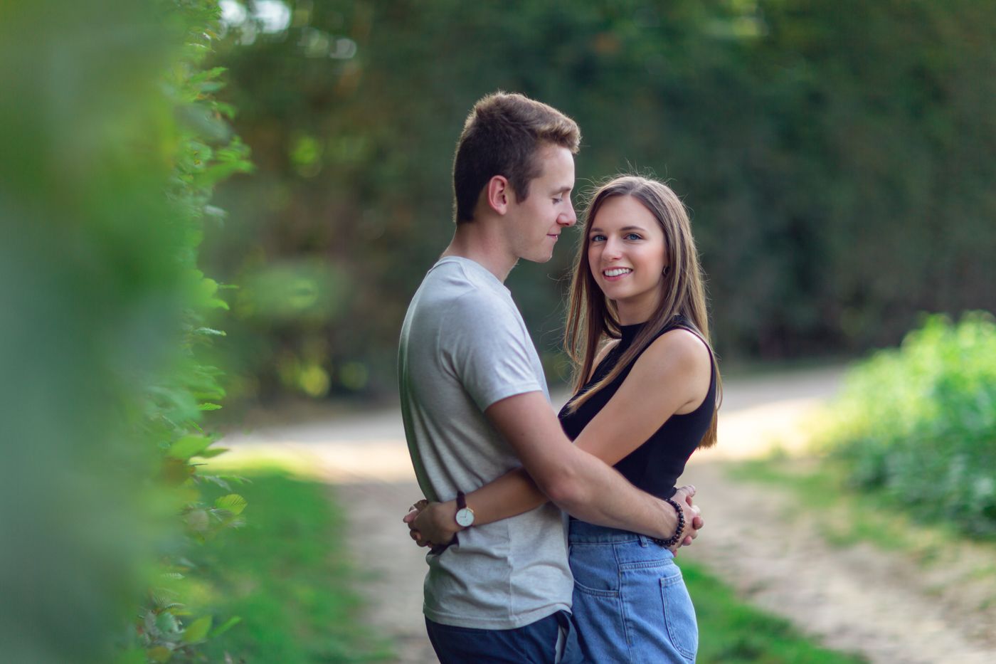 Romantic couple embracing on nature path with soft bokeh background.