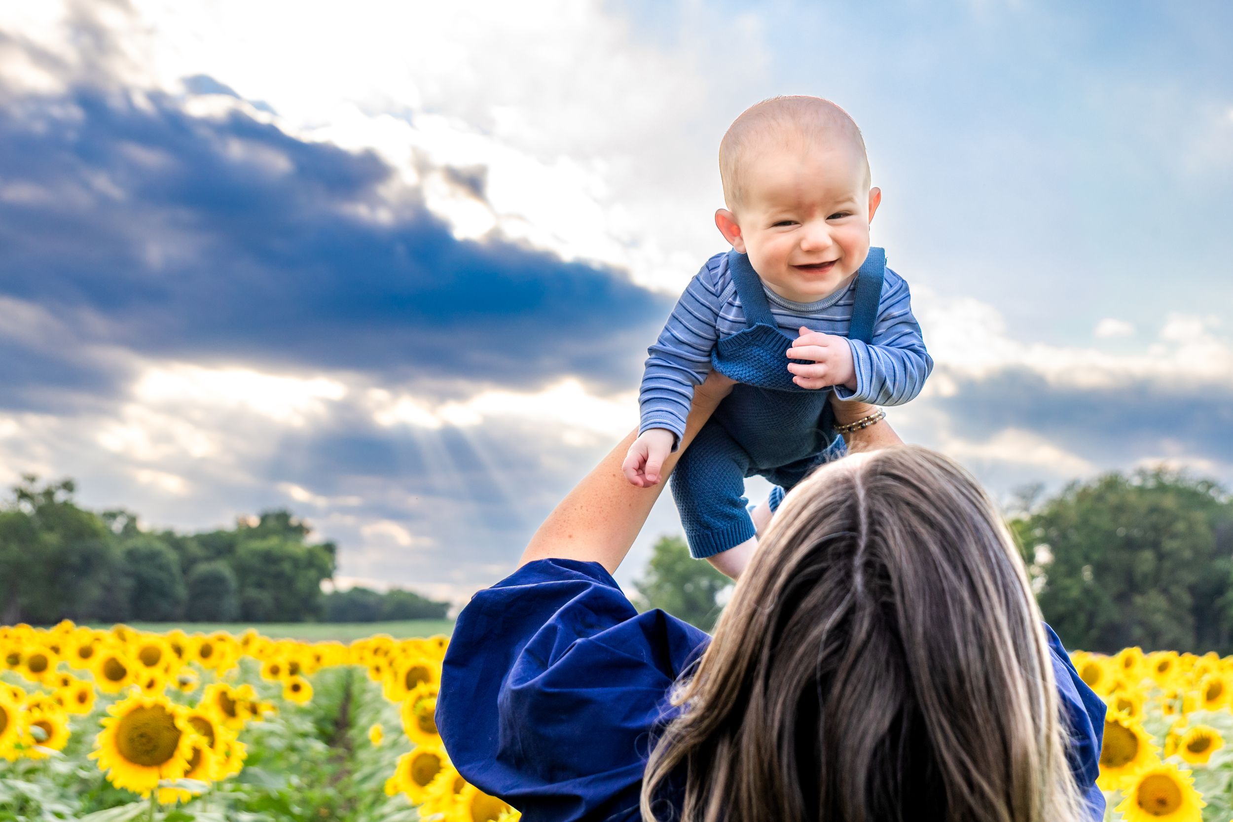 A joyful moment captured in a vibrant sunflower field against a cloudy sky at sunset.