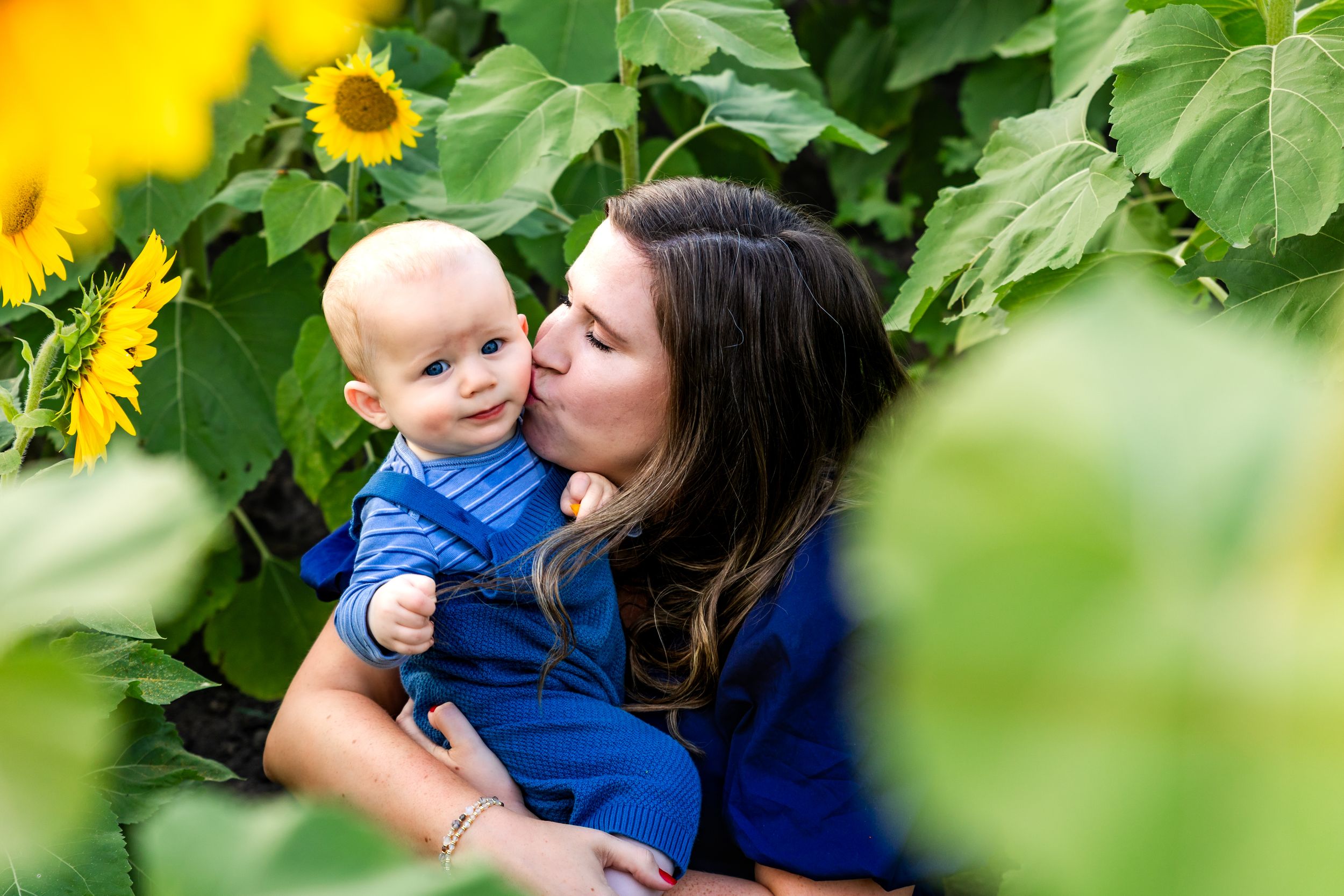 A tender moment captured in a garden with sunflowers and lush greenery in the background.
