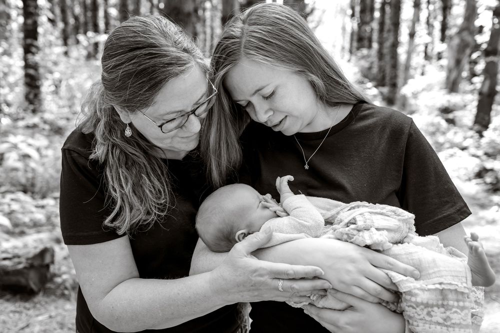 A couple in a forest setting share an intimate moment while holding their newborn baby.