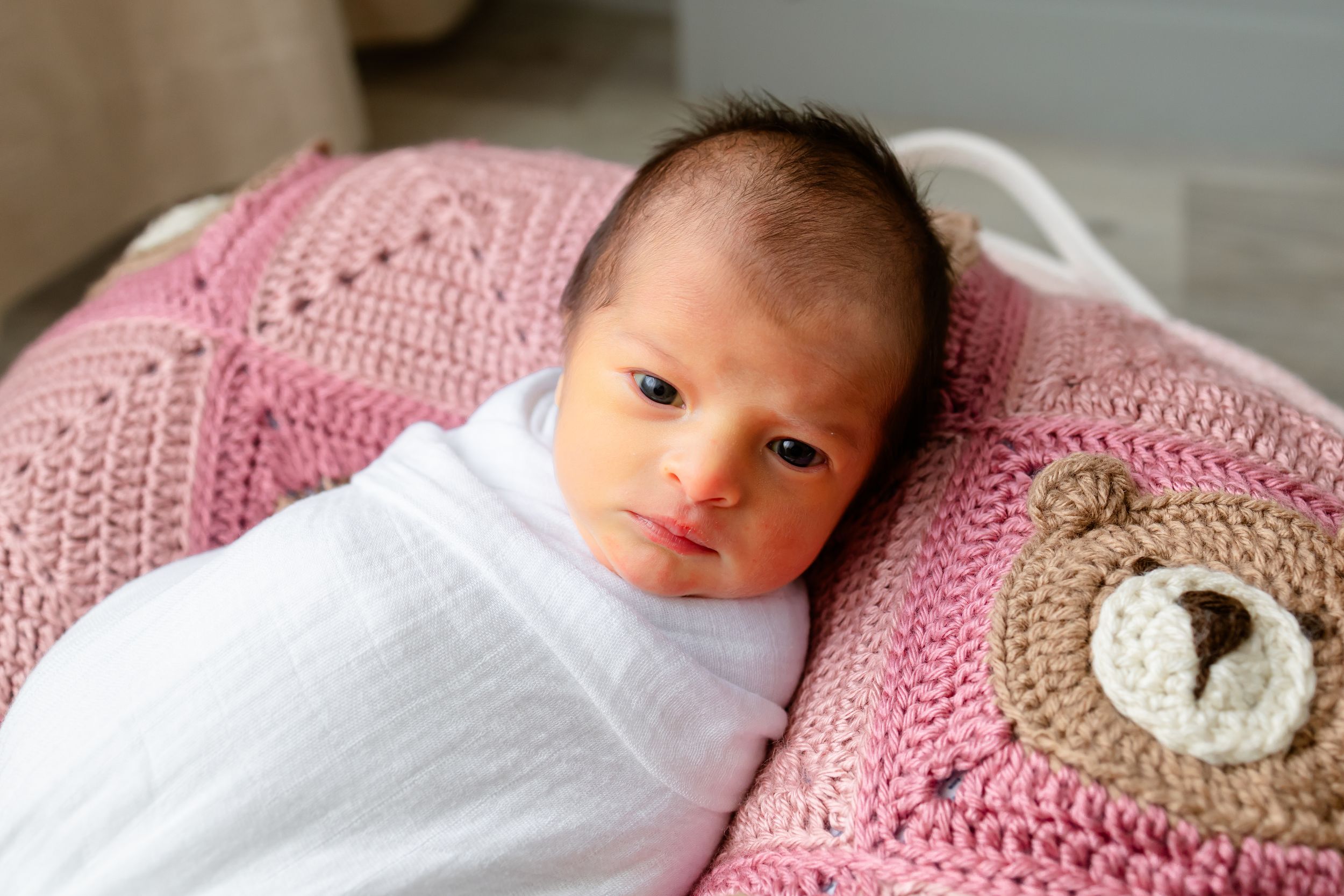 Newborn baby resting on pink and white crochet blanket with delicate details.