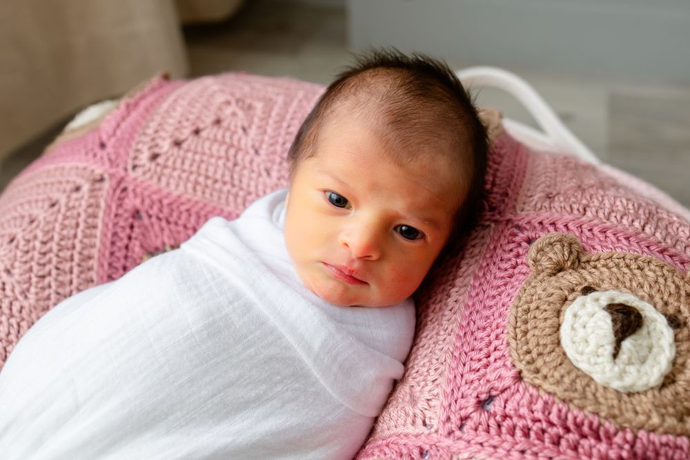 Newborn baby resting on pink and white crochet blanket with delicate details.