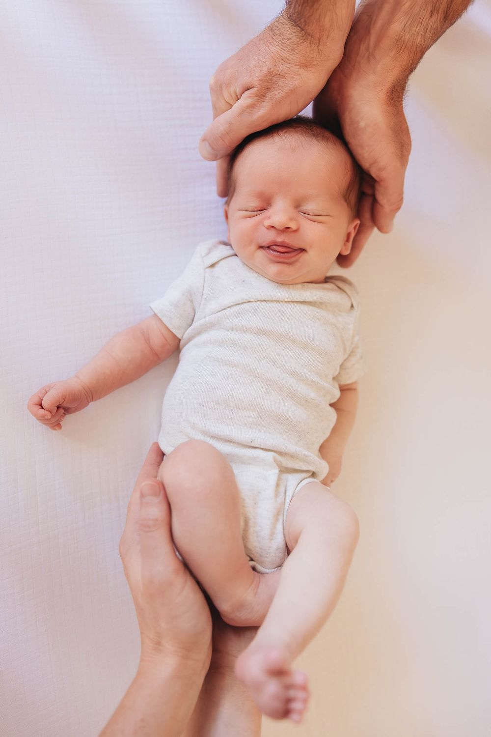 A parent's hands gently massage a sleeping baby's body on a soft white surface for infant massage therapy.