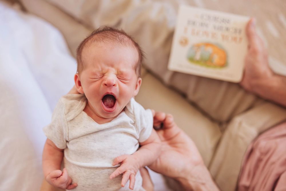 A progression of five photos showing a smiling newborn baby at different angles lying on a cushioned surface.