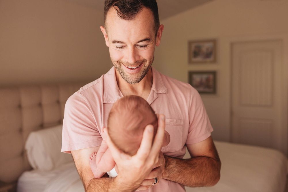 A parent tenderly holds and cuddles with a newborn baby in a warm, sunlit living room setting.