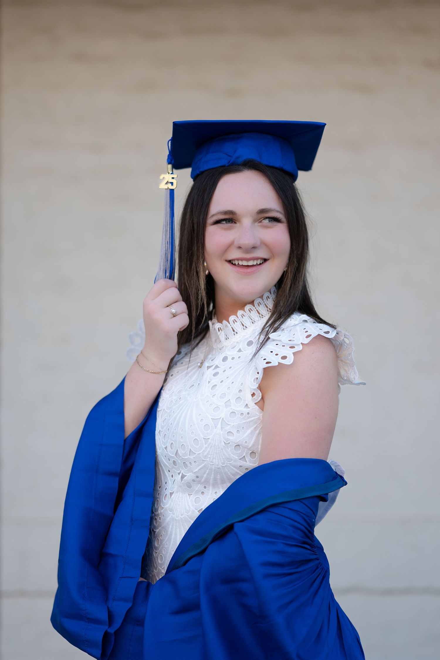 Graduate wearing traditional black cap and gown with orange accent poses outdoors on sunny day.