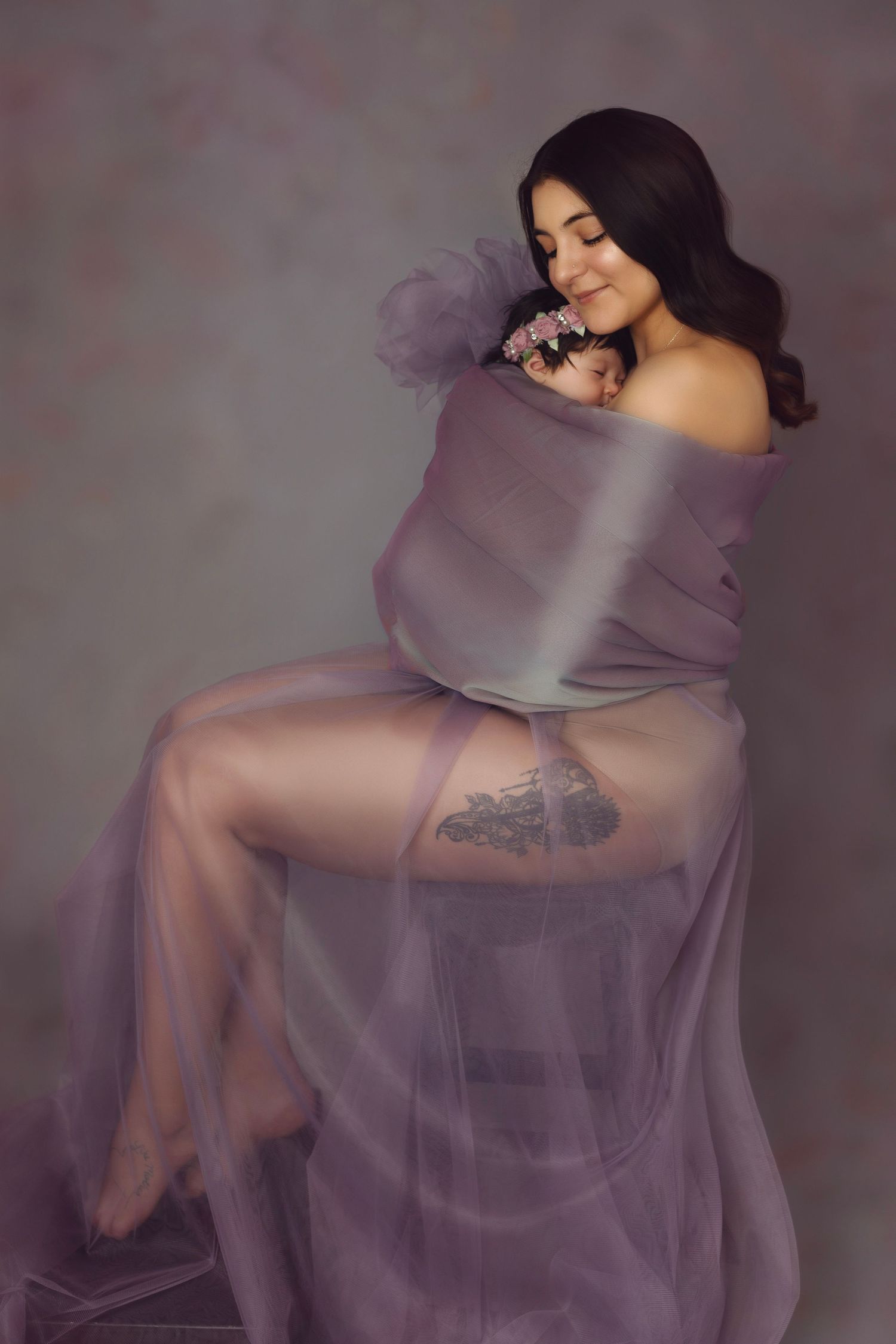 Intimate maternity portrait in sheer purple fabric with soft lighting.