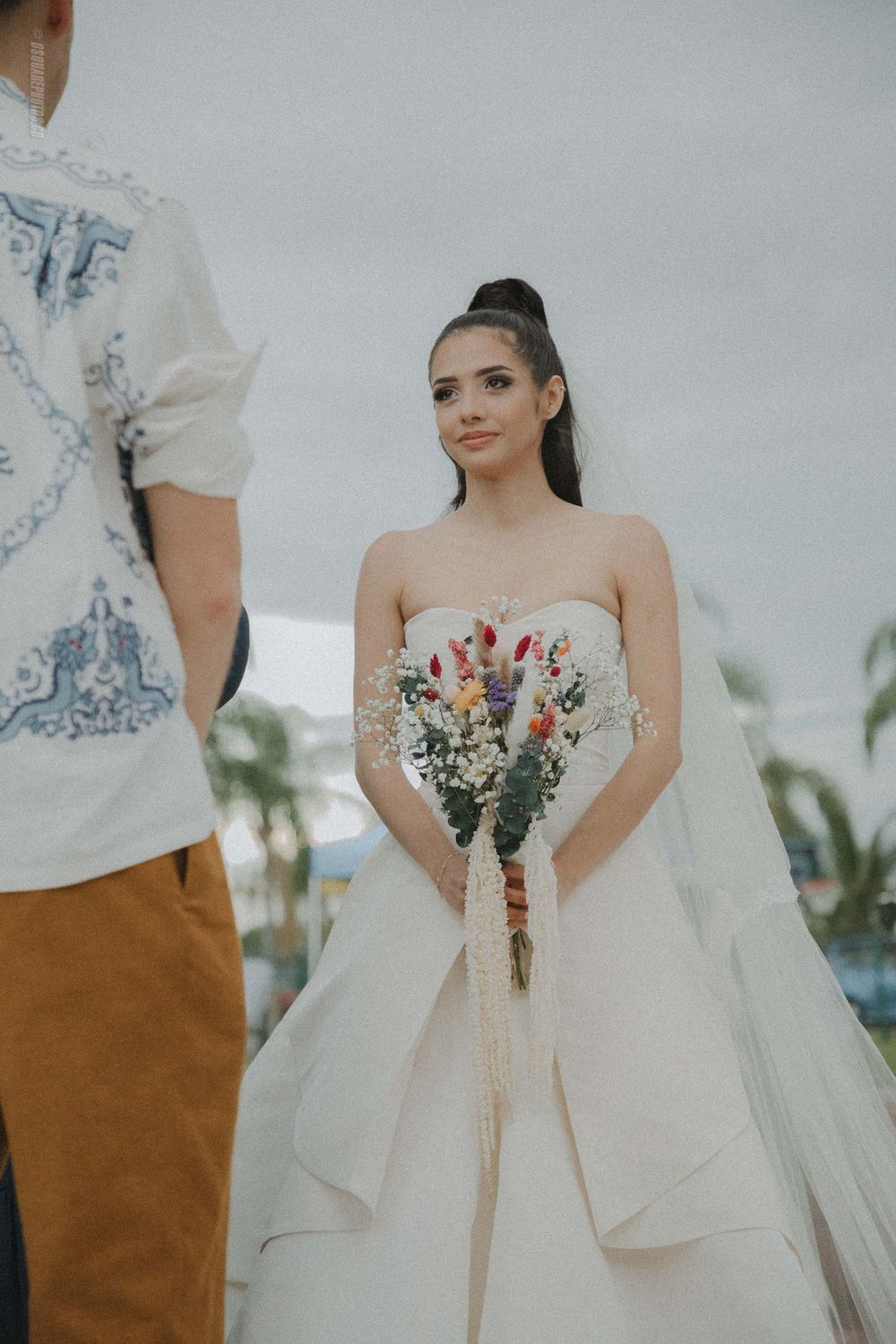 Bride in a classic strapless ballgown holds colorful bouquet during outdoor ceremony.