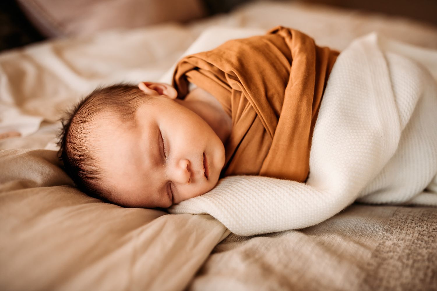 A newborn baby boy lays swaddled and wrapped in knit blankets on his parent's bed.