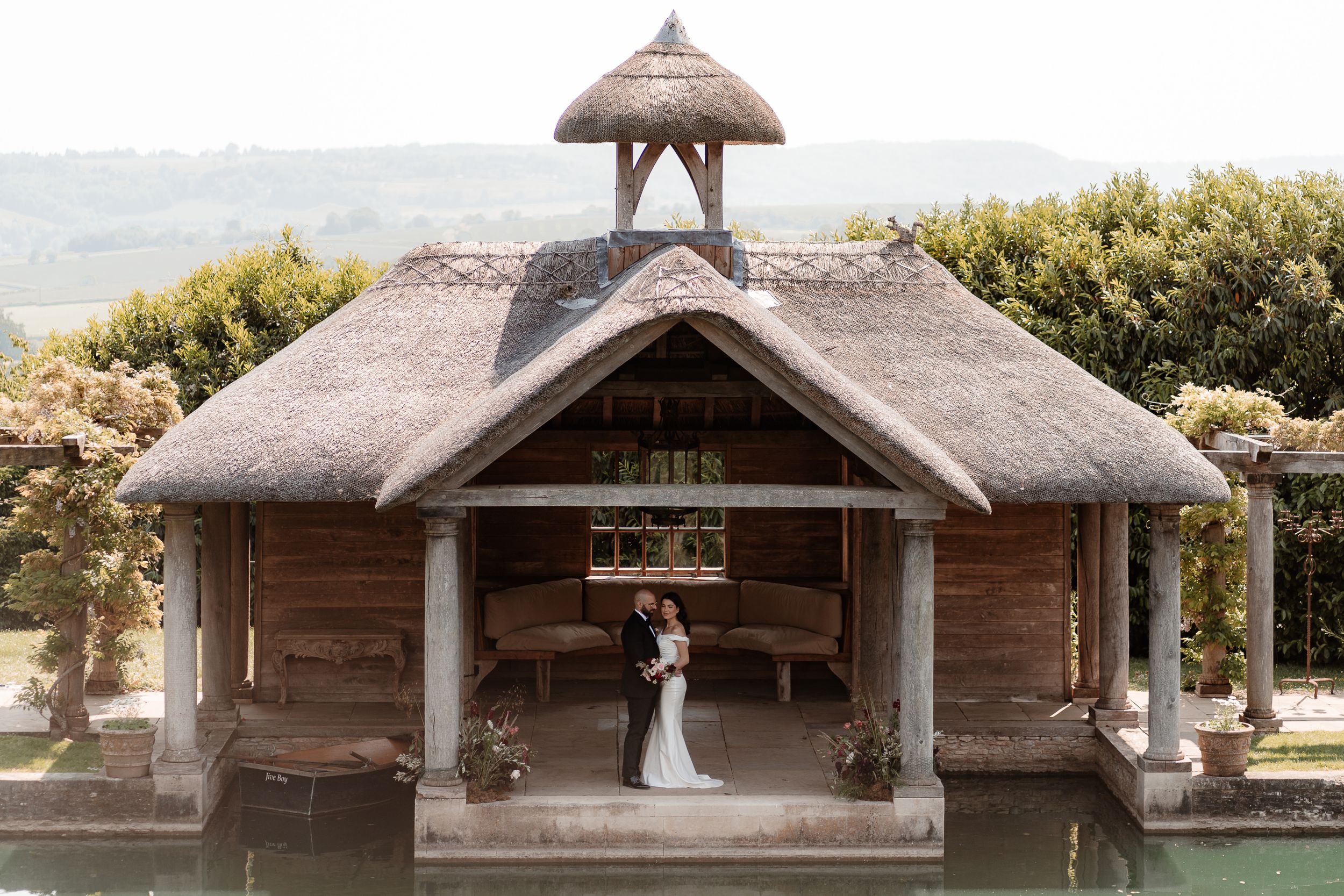 A couple stand under the thatched boathouse after their wedding at Euridge Manor, luxury Cotswolds wedding venue