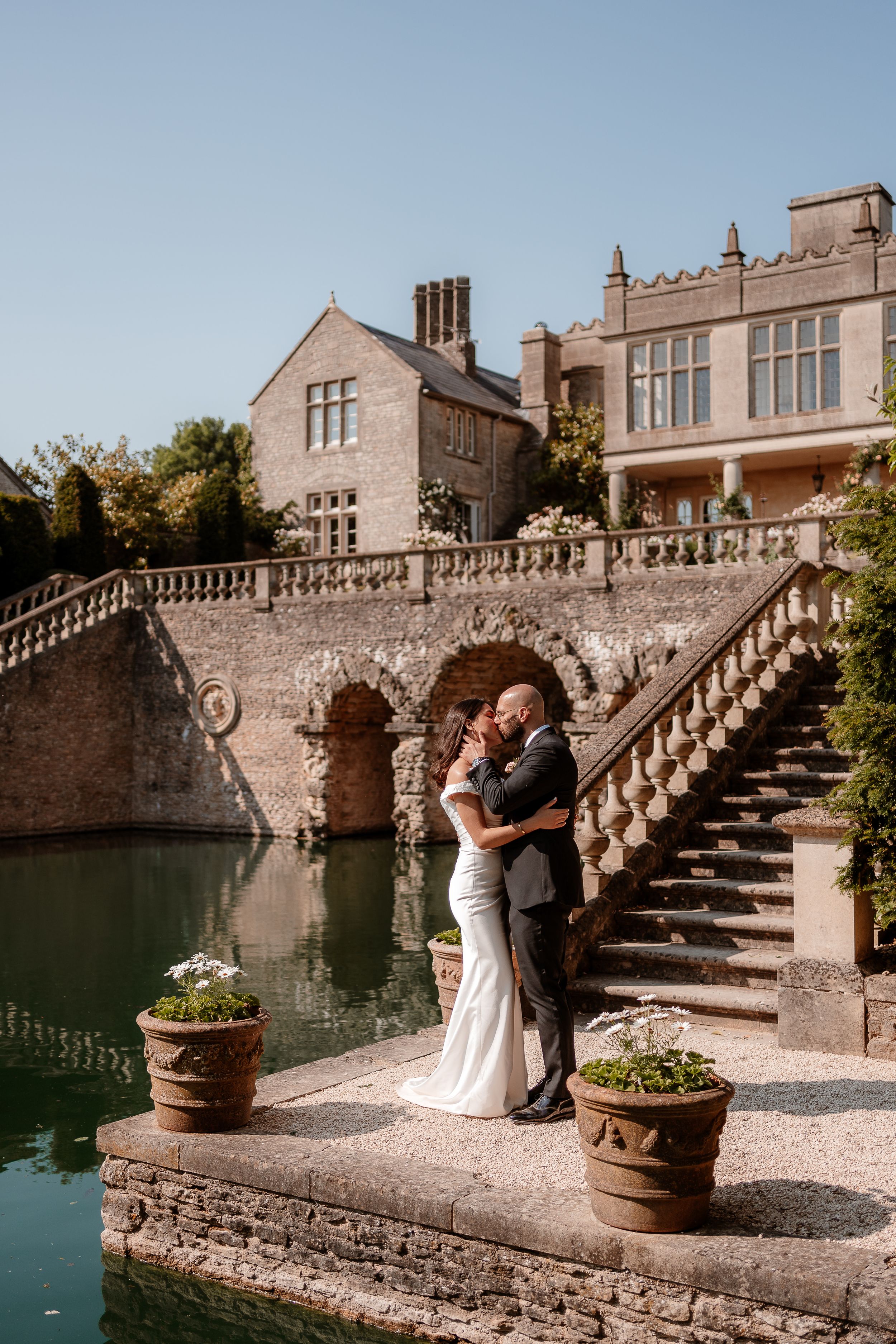 A newlywed couple stand and cuddle by the lake at Euridge Manor, luxury Cotswolds wedding venue