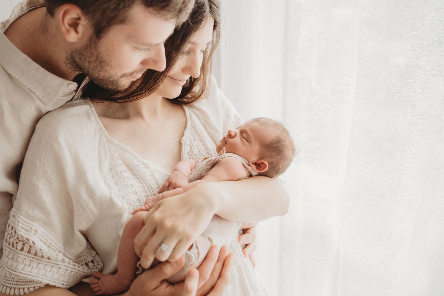 Mum and dad lovingly holding their newborn baby in their cozy Gold Coast home. The parents are smiling down at baby