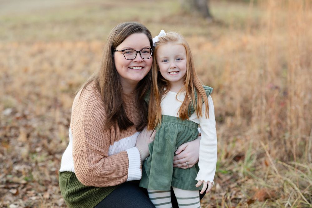 A heartwarming autumn portrait showing a parent and child in coordinating outfits sitting together in tall grass.