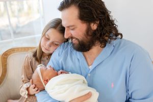 Family relaxing together on couch with newborn baby in casual home setting.