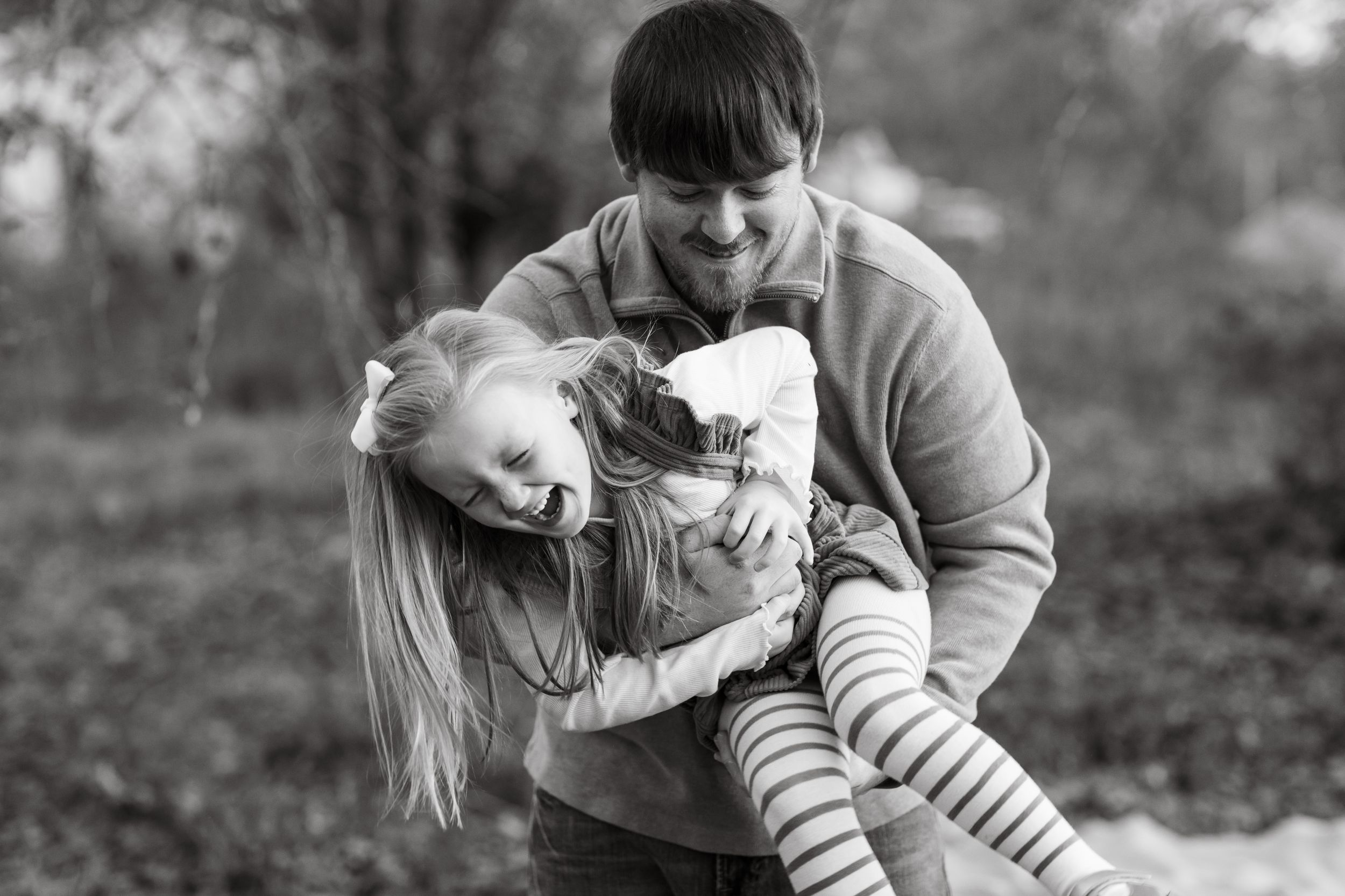 Black and white capture of parents swinging child during outdoor playtime.