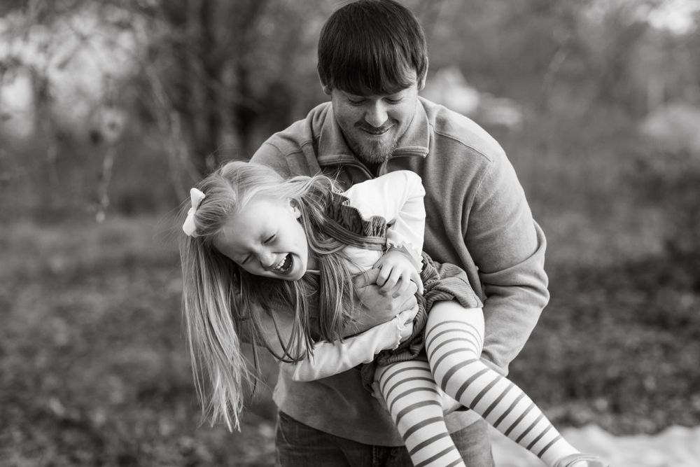 Black and white capture of parents swinging child during outdoor playtime.