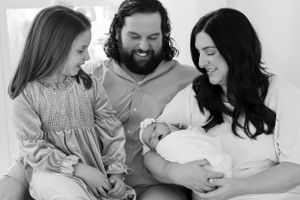 Black and white portrait of family bonding with newborn baby on couch.