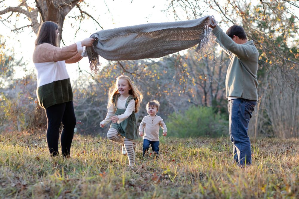 Family playing and walking together in autumn field during sunset.