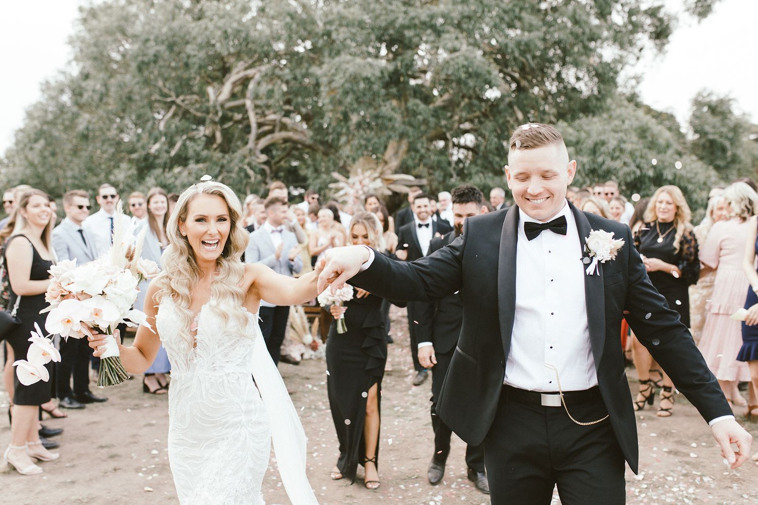 Joyful wedding celebration outdoors with guests watching as couple dances exuberantly.