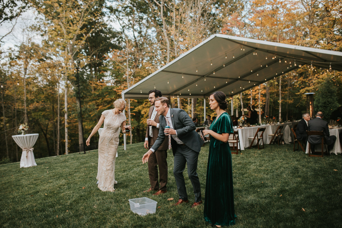 People gathered under an outdoor canopy tent during a wedding reception with fall foliage.