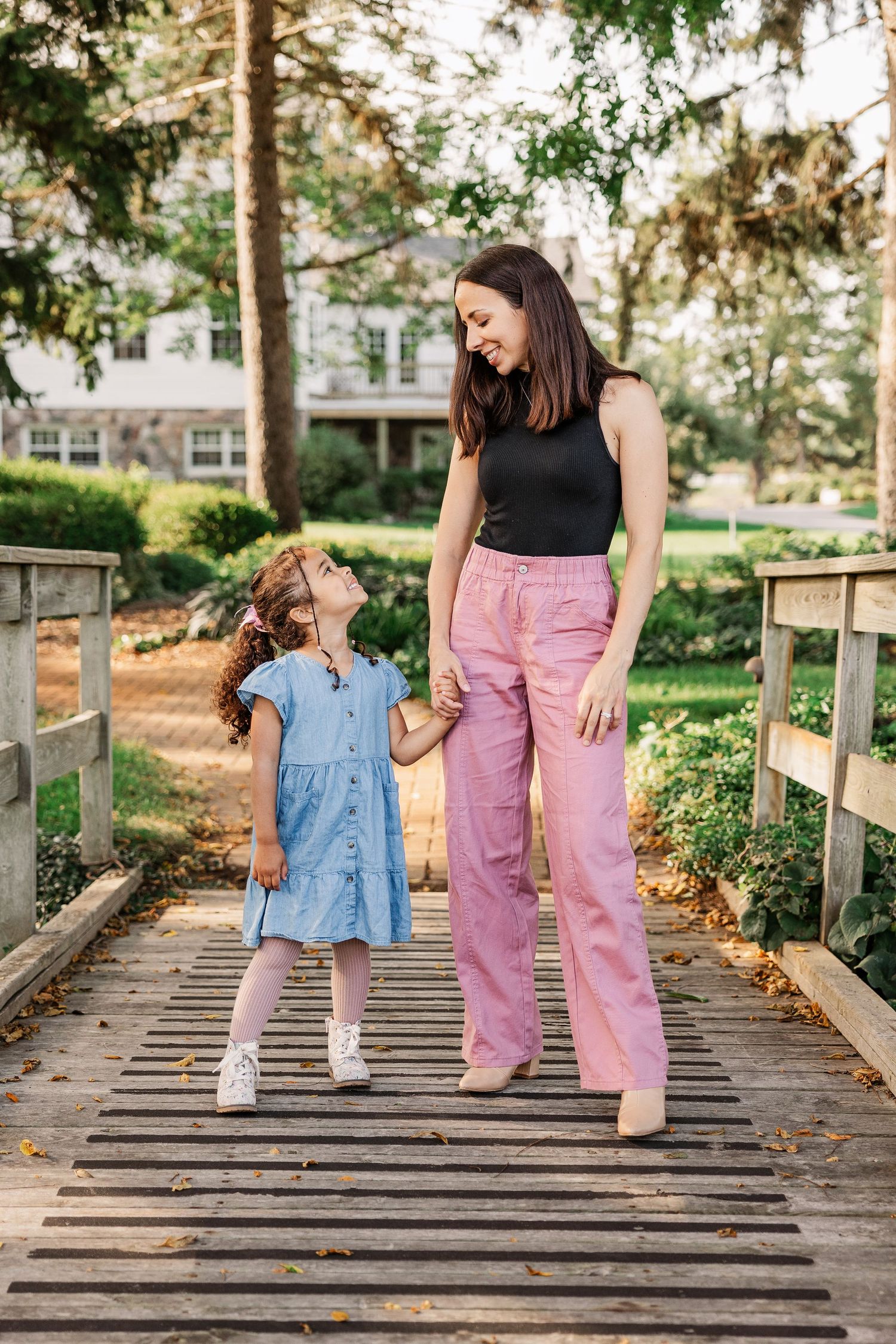 Parent and child share a sweet moment while walking together on a wooden bridge in a park.