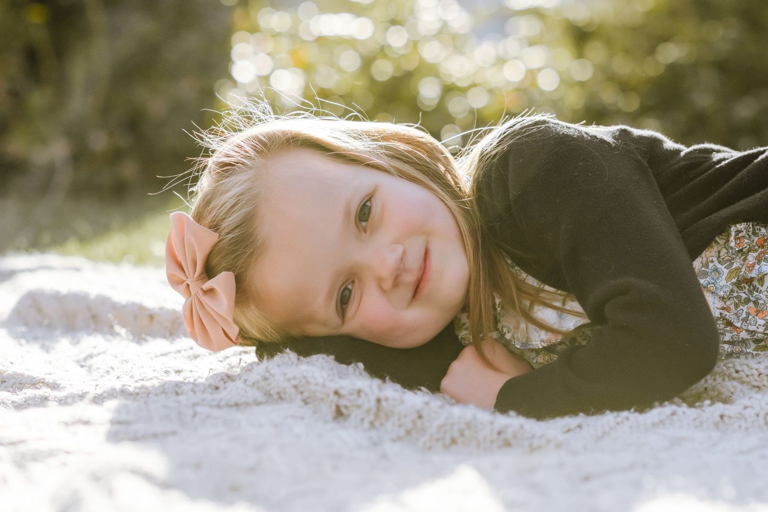 young girl laying down on side on blanket looking and smiling at camera.