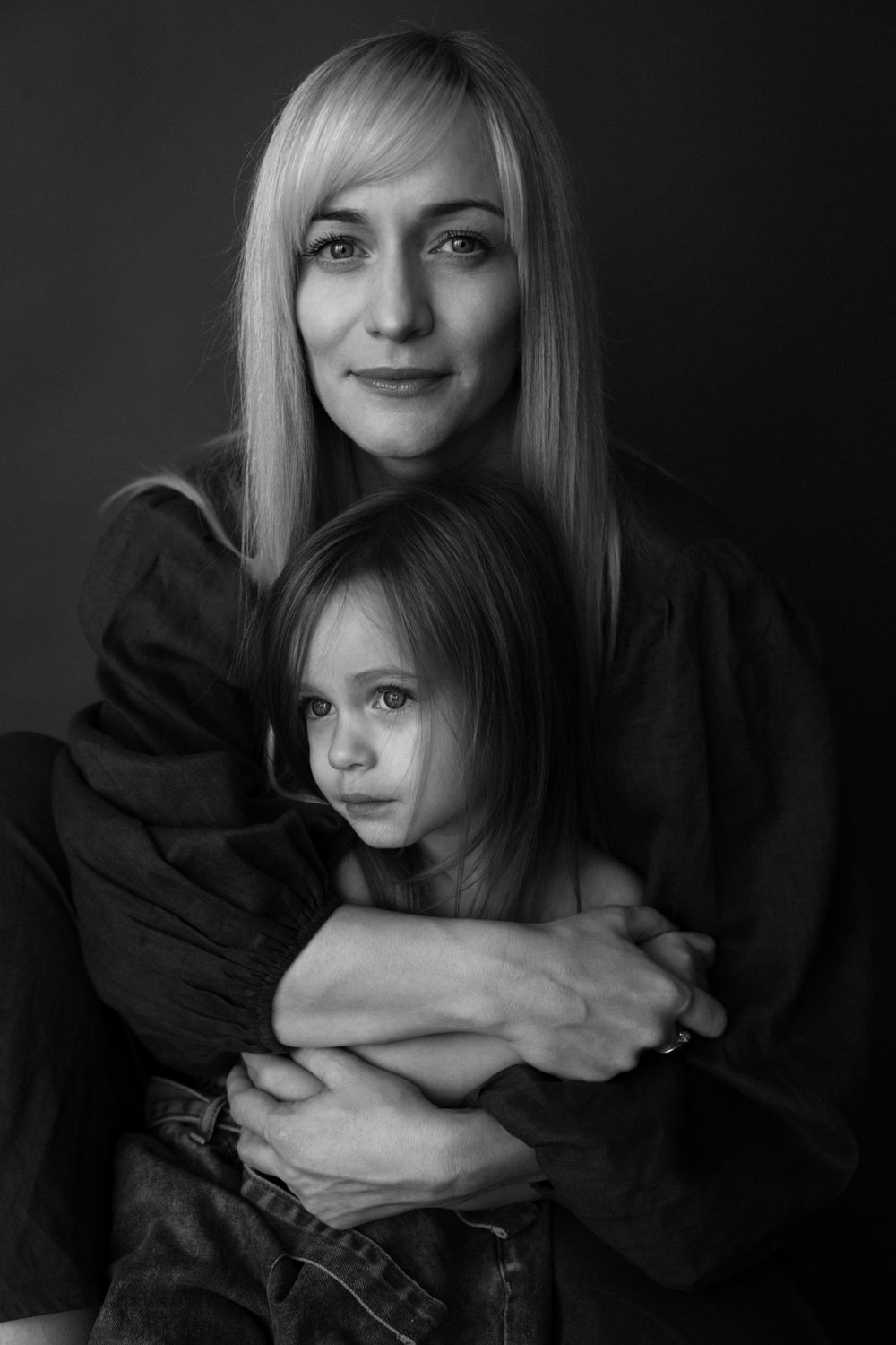 Woman holding a child in a close black and white portrait against a dark background