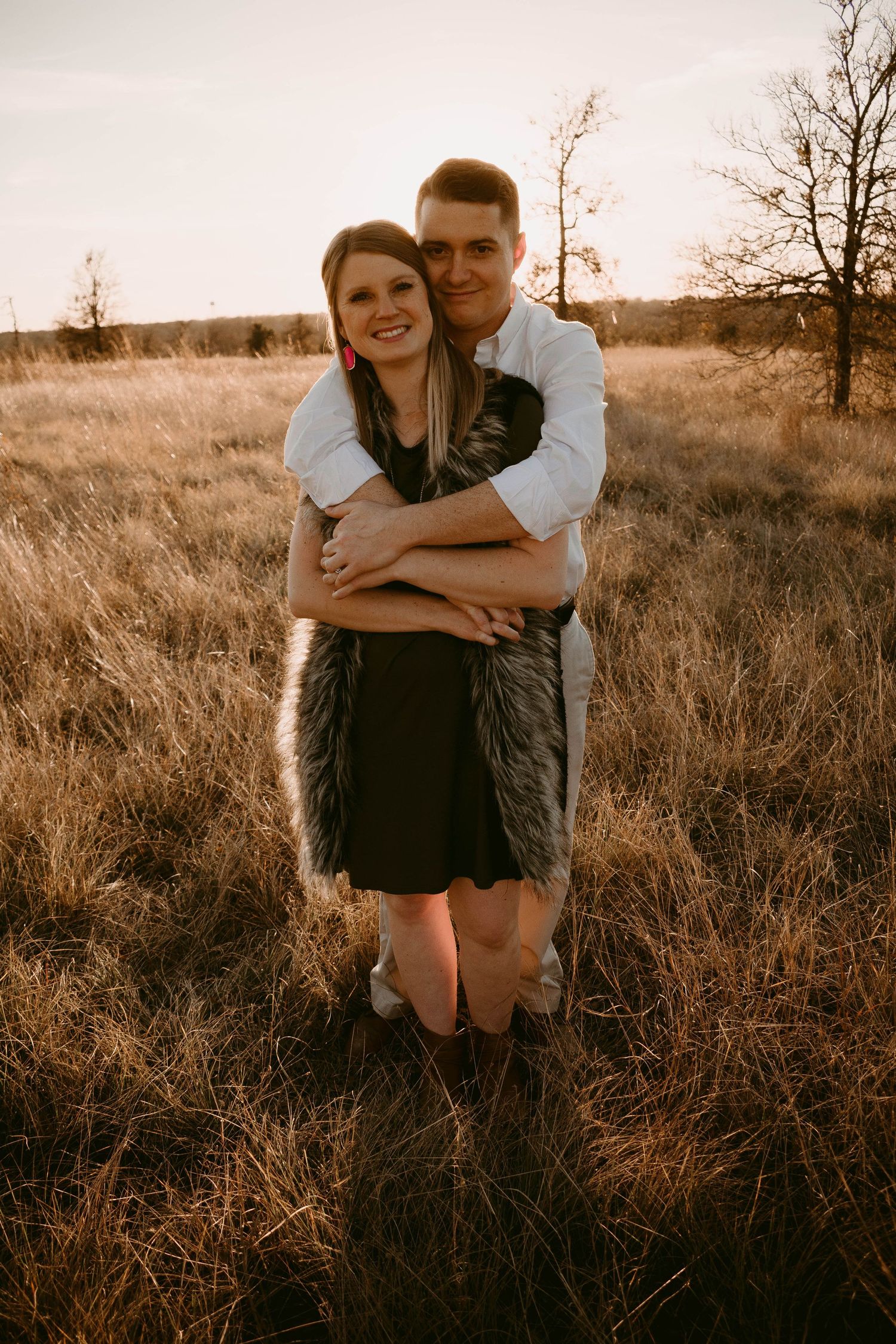 A couple embraces in a golden field at sunset with warm lighting creating a romantic atmosphere.