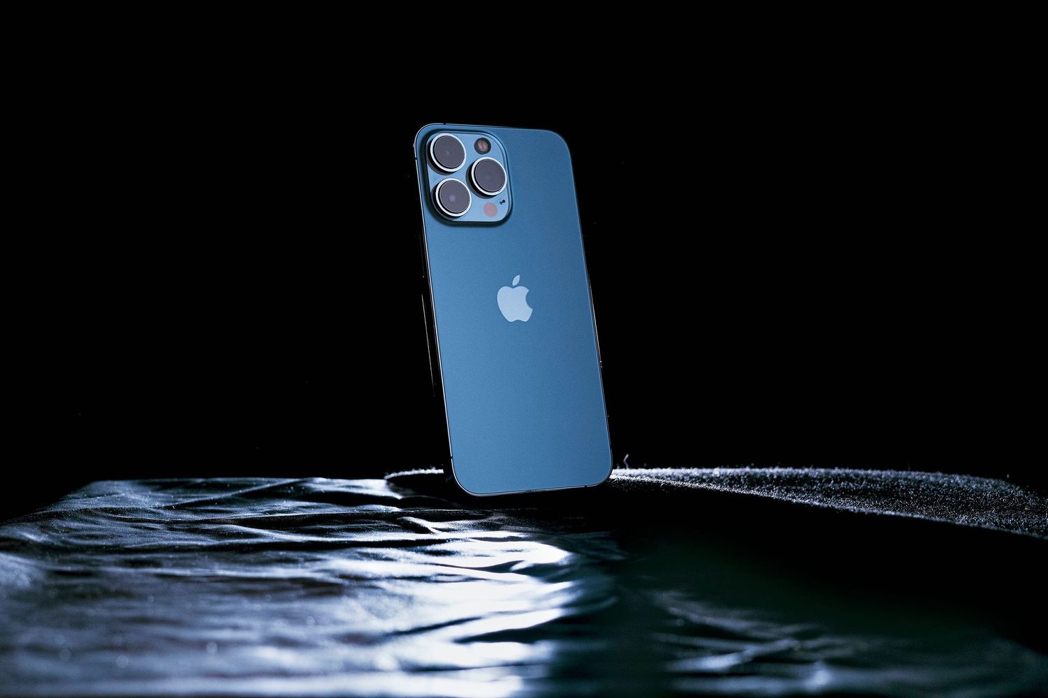 Blue iPhone models displayed in rippling water with reflective lighting effects.